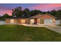 Sunset view of a single-story home boasting a well-kept lawn and an attached garage at 1109 Ne 22Nd Ave, Ocala, FL 34470