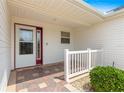 Close-up of a front porch with a white railing, brick tile flooring, and a sidelight on the front door at 2087 Bonneau Ln, The Villages, FL 32162