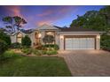 Charming single-story home with a manicured lawn, brick driveway, under a twilight sky at 6882 Sw 113Th Pl, Ocala, FL 34476