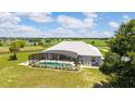 Aerial view showcases screened-in pool with lush lawn, and neighboring farm land in the distance at 5489 Nantahala Ln, Lady Lake, FL 32159