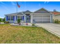 Charming single story home with manicured lawn and landscaping, an American flag, and a two-car garage at 16954 Se 93Rd Cuthbert Cir, The Villages, FL 32162
