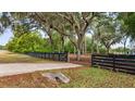 View of the property featuring a driveway, fence, mature trees, and lush green lawn at 15465 Se 113Th Street Rd, Ocklawaha, FL 32179