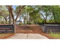 View of the property featuring a driveway, mature trees, green lawn, and metal fencing at 15465 Se 113Th Street Rd, Ocklawaha, FL 32179
