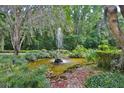 Lush garden featuring a tranquil pond with a decorative fountain, surrounded by diverse foliage and mature trees at 1300 Sw 43Rd Pl, Ocala, FL 34471