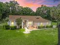 Charming single-story home featuring a manicured lawn, brick accents, and lush landscaping at sunset at 16 Count Fleet Dr, Ocala, FL 34482