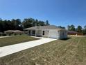 Single-story home with an attached garage and a long driveway, surrounded by lush trees and a clear blue sky at 14443 Sw 21St Pl, Ocala, FL 34481