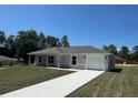 Single-story home with an attached garage and a long driveway, surrounded by lush trees and a clear blue sky at 14443 Sw 21St Pl, Ocala, FL 34481
