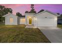 Home with manicured lawn, two car garage, and an inviting yellow front door at dusk at 12974 Se 42Nd Ct, Belleview, FL 34420