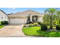 Well-maintained single-story home featuring a two-car garage, lush lawn, and mature palm tree at 3141 Roswell Rd, The Villages, FL 32162