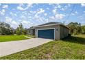 Charming single-story home with a blue garage door, gray exterior and long concrete driveway at 142 Guava Pass, Ocklawaha, FL 32179