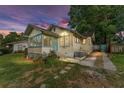 A quaint yellow single-story home is bathed in the soft glow of dusk, surrounded by lush greenery at 1434 Se Silver Springs Pl, Ocala, FL 34471