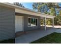 A well-lit covered front porch with a white door, gray siding, and neat landscaping at 17009 Se 60Th St, Ocklawaha, FL 32179