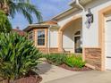 Inviting home exterior with stone accents, a covered porch, a side entry garage and verdant tropical landscaping at 1953 Hartford Path, The Villages, FL 32162