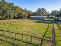 Fenced paddock leading to a blue and white horse barn set amongst green pastures and mature trees at 7563 Nw 21St St, Ocala, FL 34482