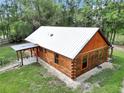 Angle view of log cabin with metal roof and covered porch, enhanced by meticulous landscaping and natural surroundings at 5630 Se 183Rd Avenue Rd, Ocklawaha, FL 32179