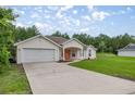 An exterior shot of a one-story home with a two-car garage and a spacious driveway, surrounded by a verdant lawn at 144 Malauka Pass, Ocklawaha, FL 32179