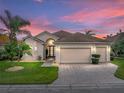 Inviting single-story home with a well-kept lawn, brick driveway, and a spacious three-car garage against a colorful sky at 4193 Stone Creek Loop, Lake Wales, FL 33859