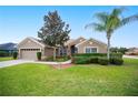 Tan house with a two-car garage, lush landscaping, and a palm tree at 359 Mandolin Ln, Winter Haven, FL 33884