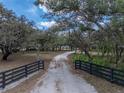 A gravel driveway flanked by a black fence, leads through mature trees to a beautiful property at 3805 Mammoth Grove Rd, Lake Wales, FL 33898