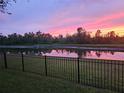 A serene evening backyard view with a fence overlooking a tranquil pond reflecting the colorful sunset at 505 Adams View Ln, Auburndale, FL 33823