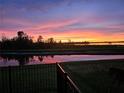 A scenic backyard view with a fence, showcasing a serene pond reflecting the vibrant sunset at 505 Adams View Ln, Auburndale, FL 33823