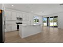 Bright kitchen features white cabinets, stainless steel appliances, island, and sliding glass doors to the backyard at 1667 Sugarbelle Cir, Mascotte, FL 34753