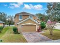 Tan two-story house with a brick paver driveway and landscaping at 4364 Fox Glen Loop, Kissimmee, FL 34746