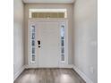 Bright entryway with a white front door flanked by sidelights and topped with a transom window, and light wood flooring at 6921 Cupseed Ln, Harmony, FL 34773