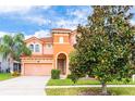 Two-story house with orange stucco and tile roof, lush landscaping, and a magnolia tree at 4525 Stella St, Kissimmee, FL 34746