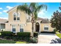 Inviting two-story home featuring a well-manicured lawn, lush landscaping, and a mature palm tree at 240 Minniehaha Cir, Haines City, FL 33844