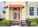 Close-up of a cheerful yellow townhome entrance with an orange-framed glass door and stylish exterior lighting at 2960 Caribbean Soul Dr, Kissimmee, FL 34747