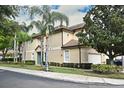 A two-story tan townhome featuring a tile roof, attached garage, and lush landscaping at 8766 The Esplanade # 23, Orlando, FL 32836