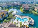 Aerial view of a beautiful community pool surrounded by palm trees and overlooking a scenic lake with fountain at 6153 Metrowest Blvd # 103, Orlando, FL 32835