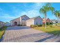 Charming single-story home with a brick driveway, arched entry, well-maintained landscaping, palm tree and an attached garage at 153 Cambridge Ave, Davenport, FL 33896