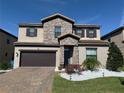 Charming two-story home with stone accents, a well-manicured lawn, and a dark brown garage door at 199 Macaulays Cv, Haines City, FL 33844