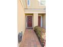 A quaint, covered front entryway featuring a red door, brick walkway, and colorful landscaping at 1737 Kato Way, Kissimmee, FL 34744
