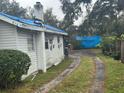 Side exterior of home with blue tarp covered roof; features a dirt driveway at 2316 W Parker St, Lakeland, FL 33815