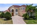 Elegant two-story home with well-manicured lawn, brick driveway, arched window, and a red tile roof at 2375 Pinehurst Ct, Davenport, FL 33837