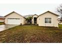 Front exterior showcasing an attached garage, driveway, mature landscaping and partial lawn at 466 Peppermill Cir, Kissimmee, FL 34758