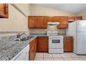 Well-lit kitchen featuring granite countertops, stainless steel sink, white appliances, and wood cabinets at 86 Pine Island Cir, Kissimmee, FL 34743