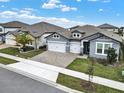 View of a gray single-story house with a three-car garage, attractive landscaping, and a brick-paved driveway at 2768 Matera Dr, St Cloud, FL 34771