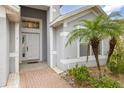 Close-up of the front door with decorative sidelights and a brick walkway surrounded by palm trees and shrubs at 105 Winchester Ln, Haines City, FL 33844