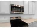 Close-up of the stainless steel microwave and oven with white quartz countertops and modern white cabinets at 1122 Olivine Ave, Dundee, FL 33838