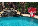 Bright turquoise swimming pool with rock waterfall detail and an attached basketball hoop at 1057 Castle Pines Ct, Reunion, FL 34747