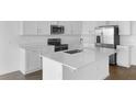 Modern white kitchen featuring an island with quartz countertops, stainless steel appliances, and wood-look tile flooring at 2967 Gavin Sky Dr, Kissimmee, FL 34744