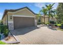 Well-maintained home featuring a brick driveway, a brown garage door, and mature landscaping at 164 Montoro Ln, Davenport, FL 33837