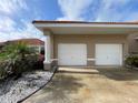 Two-car garage featuring white doors, stucco siding, and a lush, tropical landscaped entrance at 1750 Saint Tropez Ct, Kissimmee, FL 34744