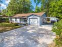 Single-story home with a long driveway, attached garage, and covered parking area, surrounded by mature trees at 412 Noya Ln, Apopka, FL 32712