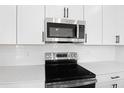 Close-up of stainless steel microwave and range featuring white cabinets, quartz countertops, and tile backsplash at 1067 Cloud Ridge Ct, Mount Dora, FL 32757