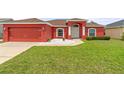 Beautiful exterior view with a lush green lawn, red facade, and attached garage at 318 Highland Meadows Dr, Davenport, FL 33837